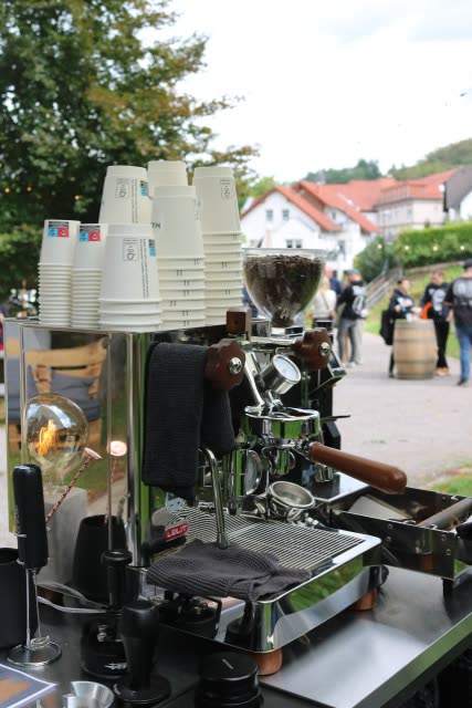 Chrome-Espressomaschine von Madynio mit Milchschaum und Gästen im Hintergrund