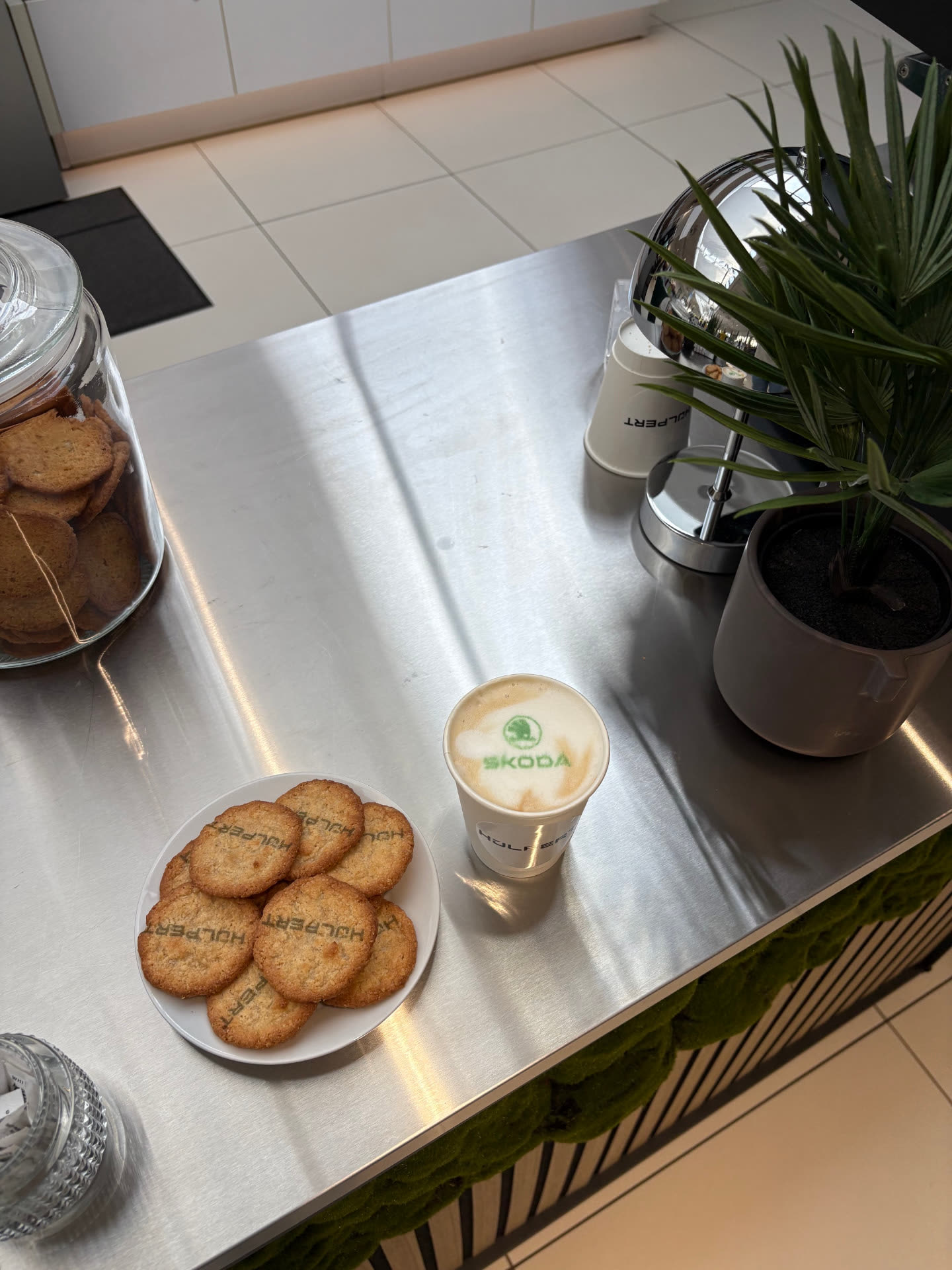 Cappuccino mit grünem Škoda-Logo im Milchschaum und Kekse mit Hülpert-Logo, bedruckt mit dem Madynio Kaffeedrucker