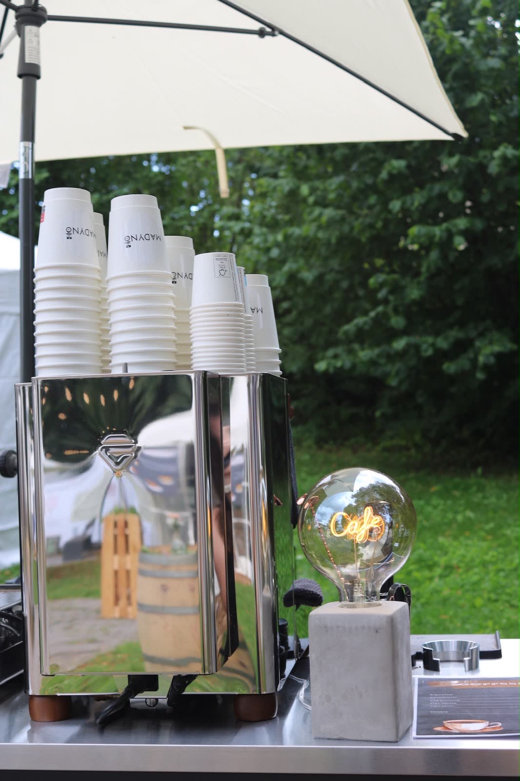 Chrome-Espressomaschine mit Madynio To-Go-Bechern und leuchtender Café-Glühbirne